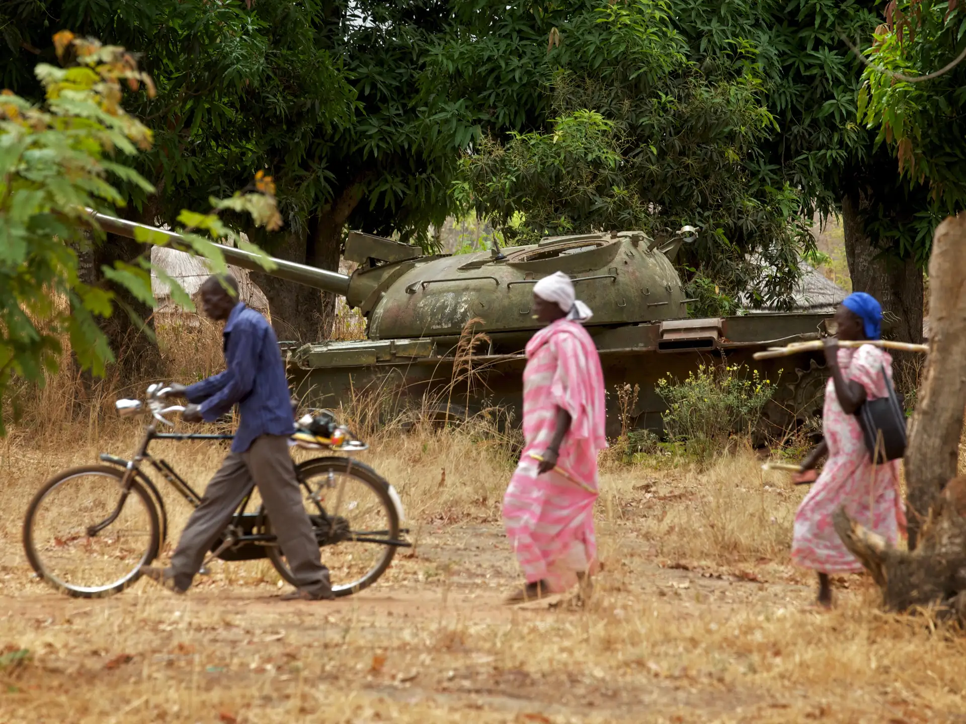 Africa - South Sudan - Community members walk past an old tank